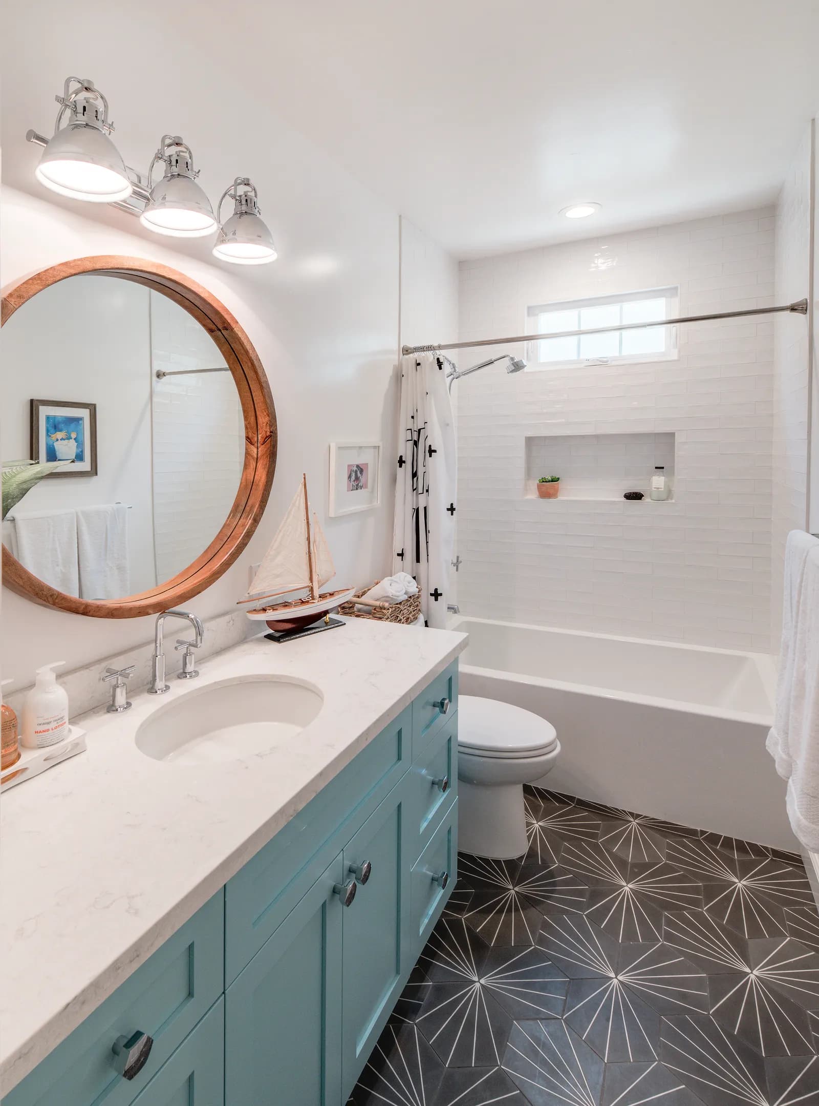 Bathroom with a teal shaker vanity, round wood mirror, white subway tile tub surround, and starburst hex tile floor.