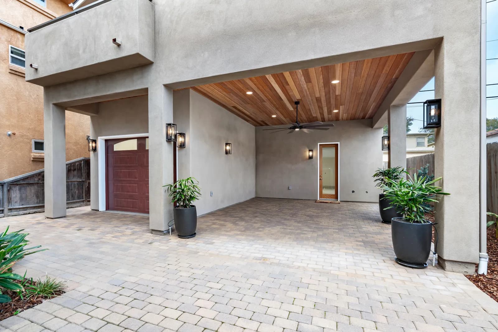 Contemporary stucco home with a covered paver courtyard, wood-plank ceiling, and lantern sconces.