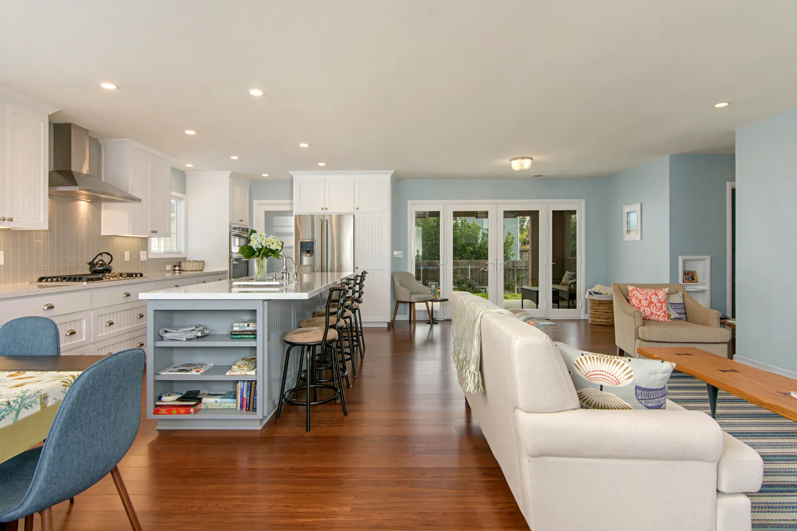 An open-plan space with a white kitchen, gray island with bookshelves, and a light blue living area beyond.